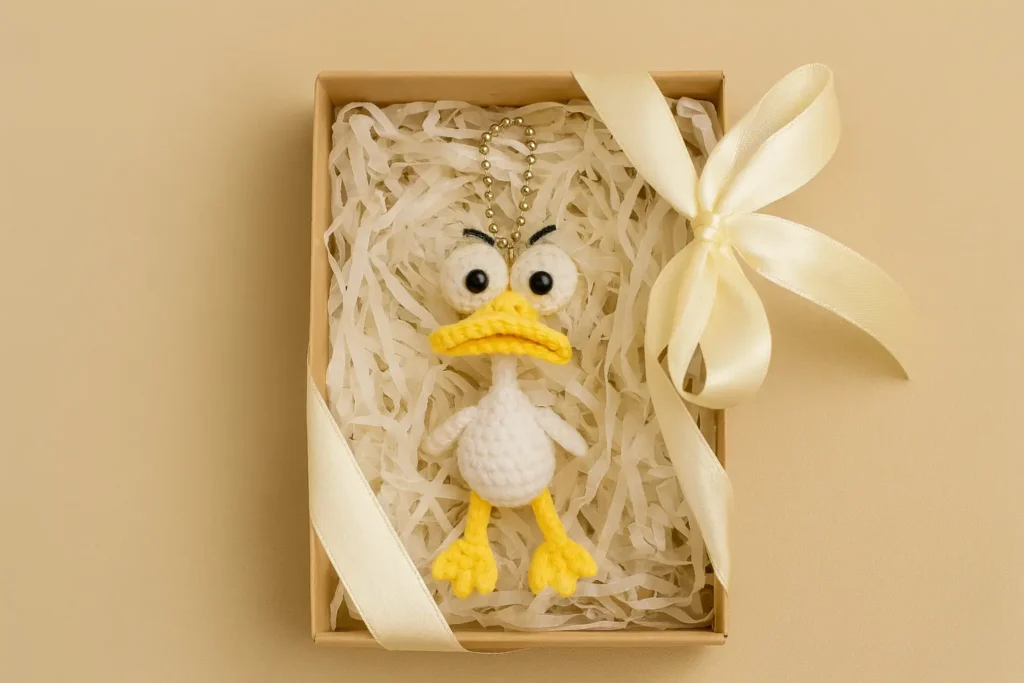 Amigurumi duck keychain in a gift box with satin ribbon and paper shreds.