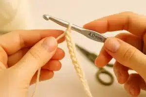 Hands showing how to single crochet with cream yarn and a 4.0 mm crochet hook