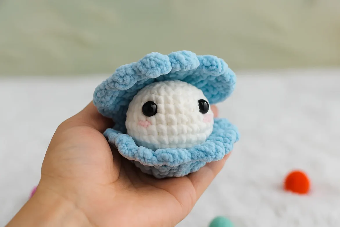 Blue crochet clam shell pattern with white pearl held in a hand