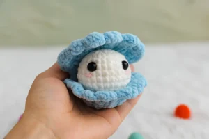Blue crochet clam shell pattern with white pearl held in a hand