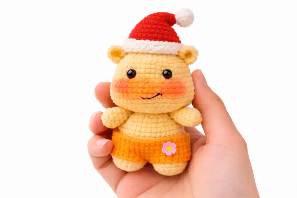 Hand holding Lulu the Capy-Hippo amigurumi wearing a mini Santa hat, made from a capybara crochet pattern free.