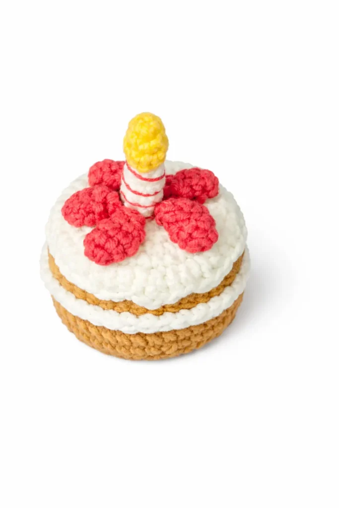 Crochet birthday cake top view with drippy frosting, candle, and strawberries in a Jellycat-inspired mini keychain style