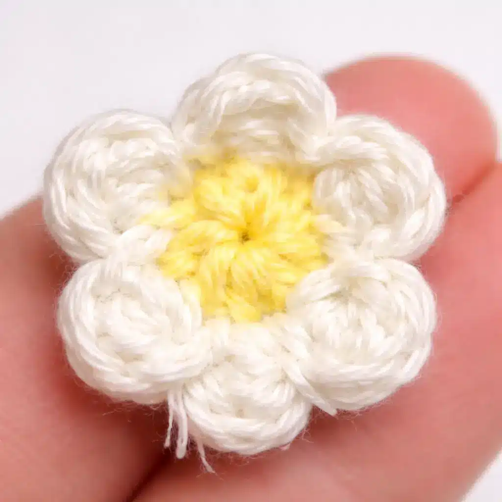 Flower embellishment step for pastel caterpillar crochet pattern with white petals and yellow center