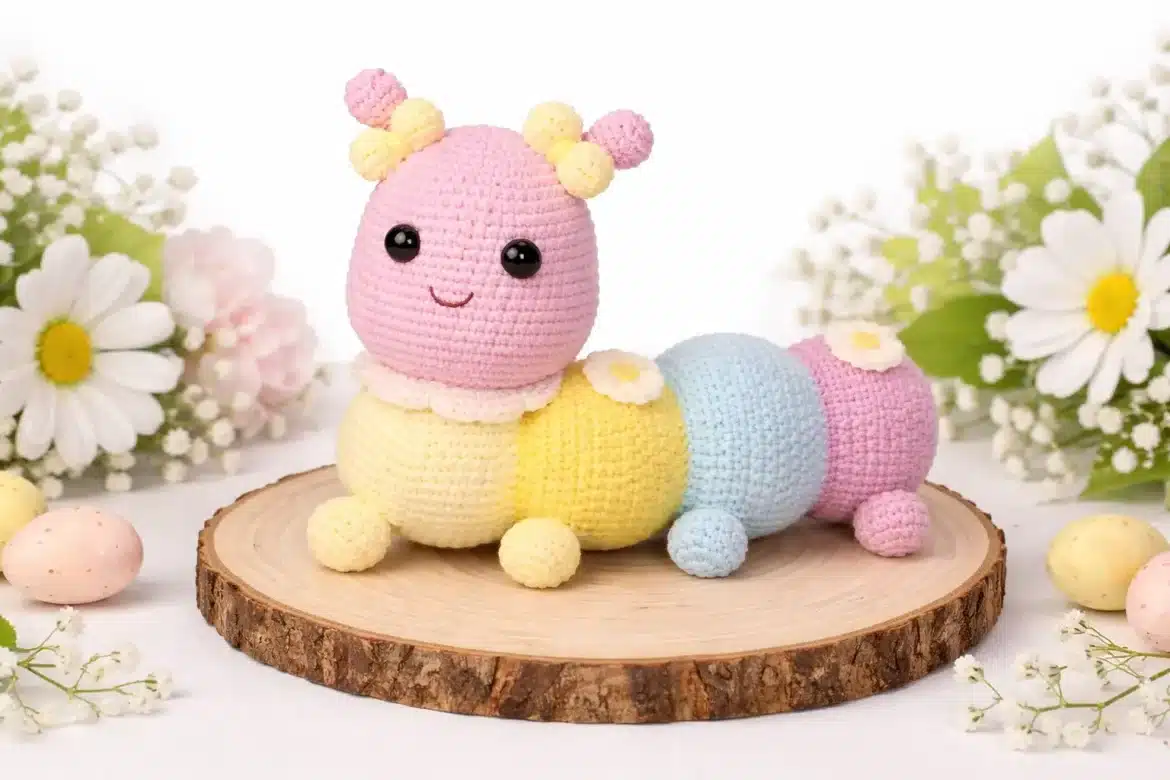 Pastel caterpillar crochet pattern final amigurumi displayed on a wooden slice with spring flowers