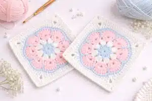 Two finished pastel floral granny square crochet pattern motifs styled with yarn and hook