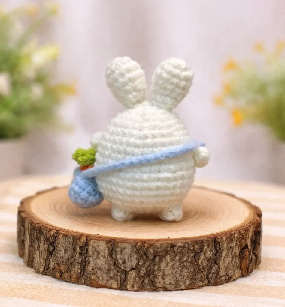 Back view of mini bunny with carrot bag crochet pattern on a wood slice